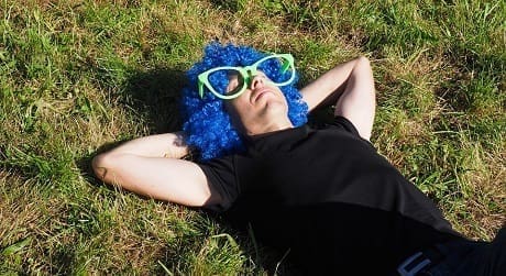 man met blauwe pruik en groene bril ligt in het gras